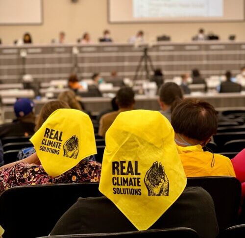 Residents wait to give public comment at a CARB board meeting, wearing yellow bandanas.